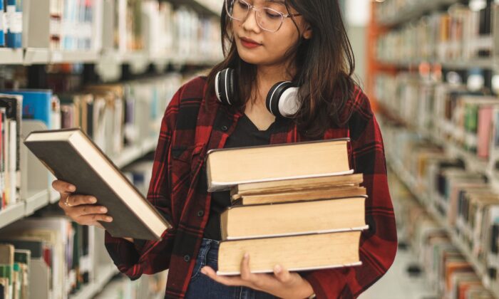 Female Student Holding Pile Of Books And Searching Book