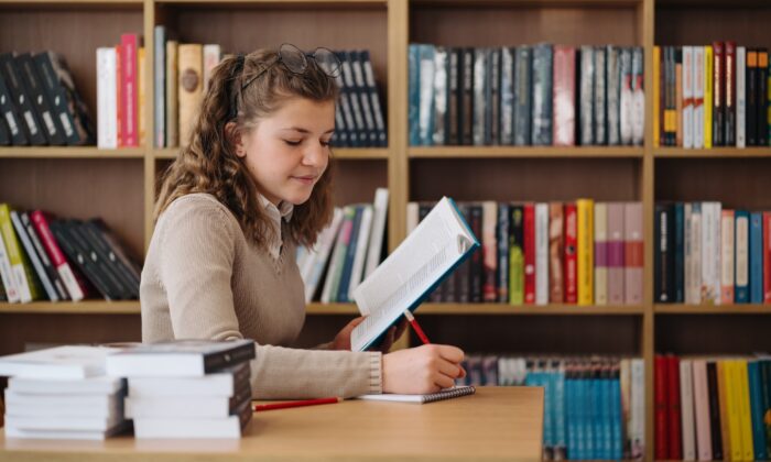 Girl Studying Among Books Sitting At The Desk Among Books